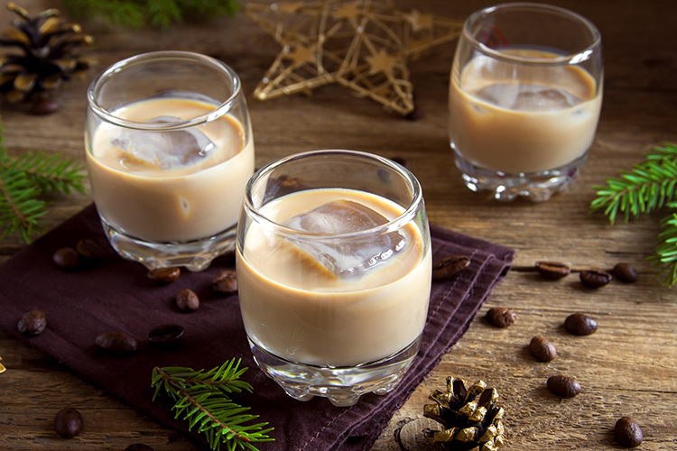 Irish cream coffee liqueur with ice, Christmas decoration and ornaments over rustic wooden background - homemade festive Christmas alcoholic drink