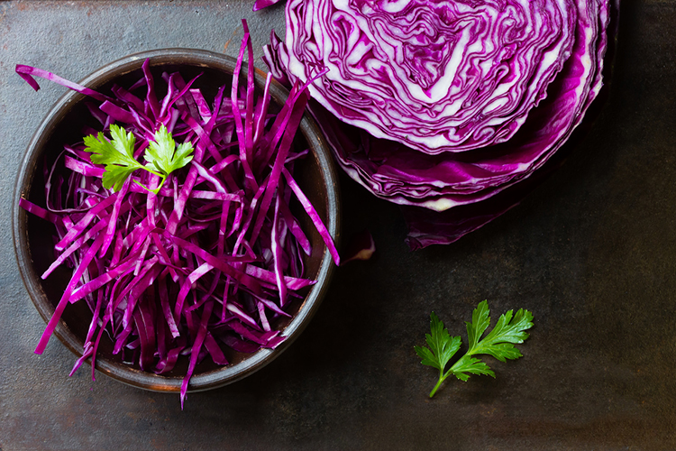 Shredded red cabbage in clay bowl on black background. Vegetarian healthy food. Top view